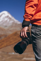 closeup photo of hiker photographer's hand holding DSLR camera against Caucasus mountains background