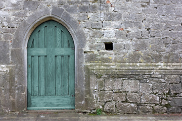 Turquoise colored wooden back door on an exterior wall of a gothic church