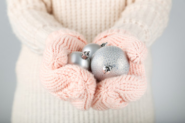 Hands in knitted mittens holding christmas baubles on grey background