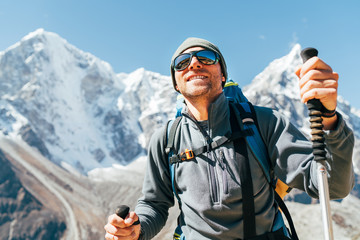 Portrait of smiling Hiker man on Taboche 6495m and Cholatse 6440m peaks background with trekking poles, UV protecting sunglasses. He enjoying mountain views during Everest Base Camp trekking route. - obrazy, fototapety, plakaty
