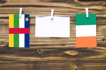 Hanging flags of Central African Republic and Ireland attached to rope with clothes pins with copy space on white note paper on wooden background.Diplomatic relations.