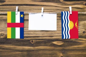 Fototapeta na wymiar Hanging flags of Central African Republic and Kiribati attached to rope with clothes pins with copy space on white note paper on wooden background.Diplomatic relations.