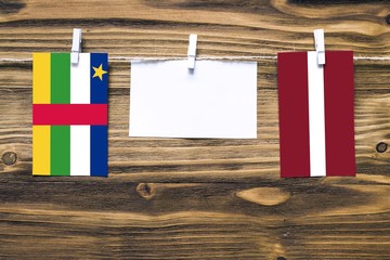 Hanging flags of Central African Republic and Latvia attached to rope with clothes pins with copy space on white note paper on wooden background.Diplomatic relations.