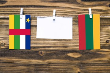 Hanging flags of Central African Republic and Lithuania attached to rope with clothes pins with copy space on white note paper on wooden background.Diplomatic relations.