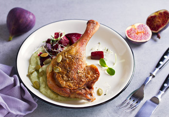 Roast duck leg with mashed green vegetables, beetroot, and pumpkin seeds on light gray background