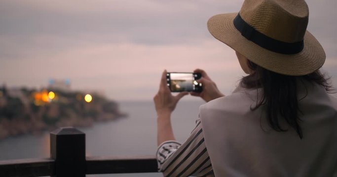 Millennial hipster woman tourist in casual outfit with photographing city harbor using application on smart phone at sunset.