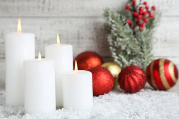 Christmas candles with bauble toys and fir tree branches on white wooden background