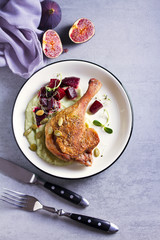 Roast duck leg with mashed green vegetables, beetroot, and pumpkin seeds on light gray background. Overhead image