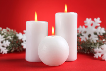 Christmas candles with snowflakes and fir tree branches on red background
