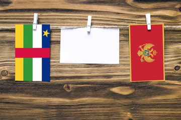 Hanging flags of Central African Republic and Montenegro attached to rope with clothes pins with copy space on white note paper on wooden background.Diplomatic relations.