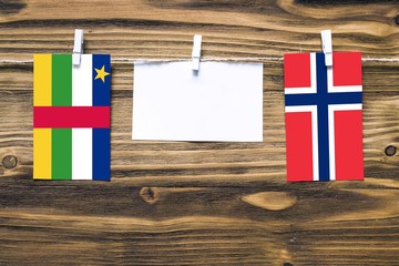 Hanging flags of Central African Republic and Norway attached to rope with clothes pins with copy space on white note paper on wooden background.Diplomatic relations.