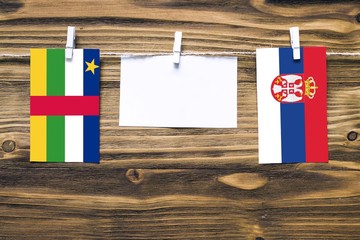 Hanging flags of Central African Republic and Serbia attached to rope with clothes pins with copy space on white note paper on wooden background.Diplomatic relations.