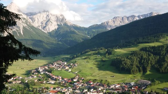 Picturesque view of Lermoos village from above with mountains and clouds in the background on a sunny day.