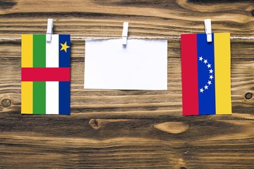 Hanging flags of Central African Republic and Venezuela attached to rope with clothes pins with copy space on white note paper on wooden background.Diplomatic relations.