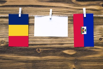 Hanging flags of Chad and Haiti attached to rope with clothes pins with copy space on white note paper on wooden background.Diplomatic relations between countries.