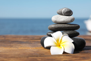 Stack of stones and flower on wooden pier near sea, space for text. Zen concept