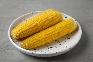 Plate with tasty boiled corn cobs on light grey table