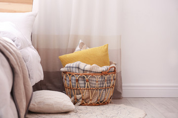 Fototapeta na wymiar Basket with blanket and pillows near bed indoors