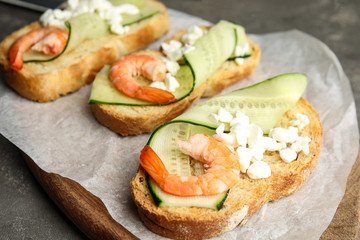Cutting board of delicious bruschettas with shrimps on grey table, closeup