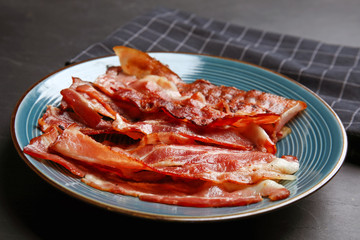 Slices of tasty fried bacon on dark table, closeup