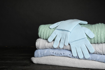 Stacked sweaters and gloves on table, closeup with space for text. Autumn clothes