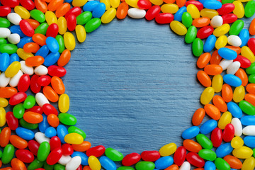 Fototapeta na wymiar Frame made of colorful jelly beans on blue wooden background, flat lay. Space for text