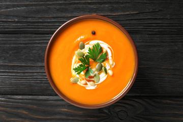 Delicious pumpkin soup in bowl on wooden table, top view