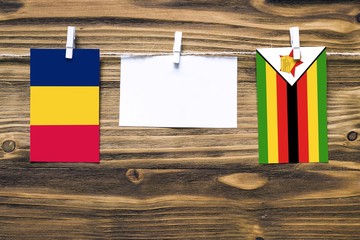 Hanging flags of Chad and Zimbabwe attached to rope with clothes pins with copy space on white note paper on wooden background.Diplomatic relations between countries.