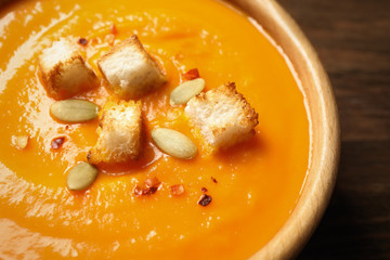 Bowl with tasty pumpkin cream soup on wooden table, closeup