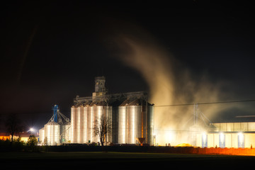 Grain dryer plant working at night.  Floating steam around. Agro farm metal elevator, tall silos...