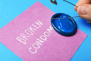 Woman piercing condom with pin on blue background, closeup. Safe sex
