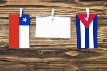 Hanging flags of Chile and Cuba attached to rope with clothes pins with copy space on white note paper on wooden background.Diplomatic relations between countries.