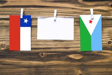 Hanging flags of Chile and Djibouti attached to rope with clothes pins with copy space on white note paper on wooden background.Diplomatic relations between countries.