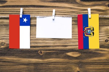 Hanging flags of Chile and Ecuador attached to rope with clothes pins with copy space on white note paper on wooden background.Diplomatic relations between countries.