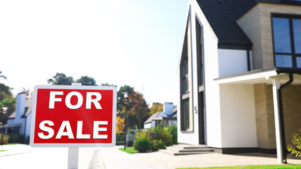Red real estate sign near house outdoors on sunny day