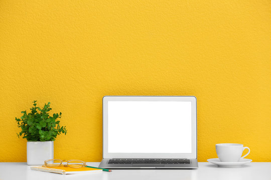 Modern laptop on desk near yellow wall, space for design. Home workplace