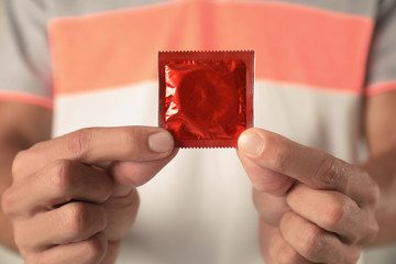 Young man holding red condom, closeup. Safe sex concept