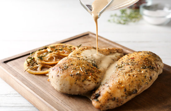 Pouring sauce onto baked lemon chicken on white wooden table