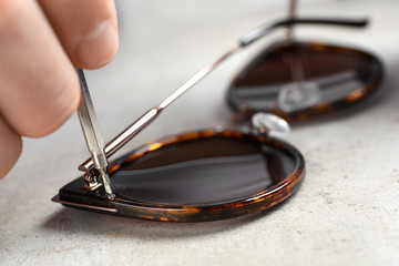Handyman repairing sunglasses with screwdriver at grey table, closeup