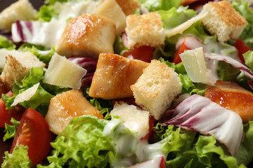 Delicious Caesar salad with fresh ingredients as background, closeup