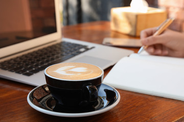 Blogger working at table in cafe, focus on cup of coffee