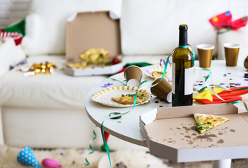 Messy table with bottle of wine and pizza indoors, space for text. Chaos after party