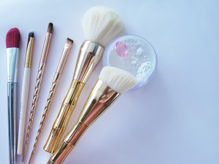 Fototapeta premium Makeup gold brushes and white powder on a white background