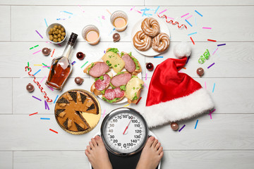 Woman using scale surrounded by food and alcohol after party on floor, top view. Overweight problem