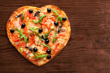 Tasty heart-shapped pizza on wooden background
