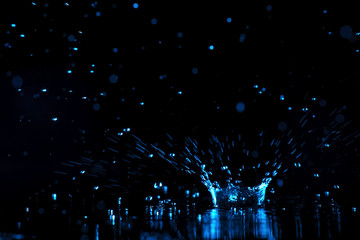 Obraz na płótnie Canvas Rain drop falling down into puddle on dark background, toned in blue