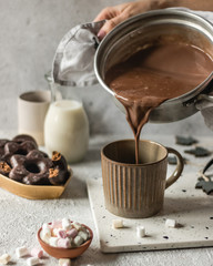 Cup of hot chocolate poured on bright background with cookies and marshmllow