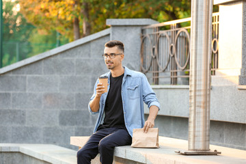 Obraz premium Young man enjoying coffee and takeaway food outdoors, urban lifestyle and casual dining experience
