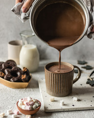 Cup of hot chocolate poured on bright background with cookies and marshmllow