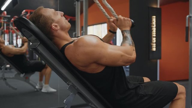 Bodybuilding concept. Muscular man doing cable rope triceps pull down exercise while working out in gym